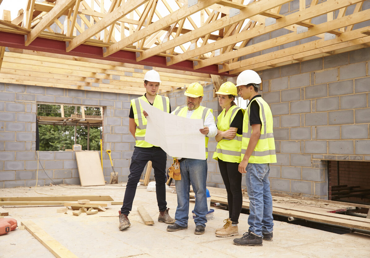 Builder On Building Site Looking At Plans With Apprentices